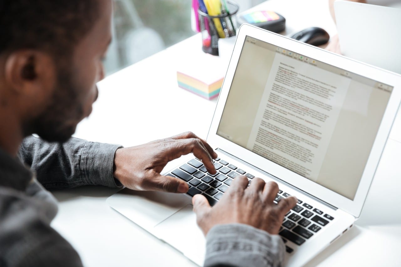 A person typing on a laptop at a desk with colorful sticky notes and office supplies in the background 
